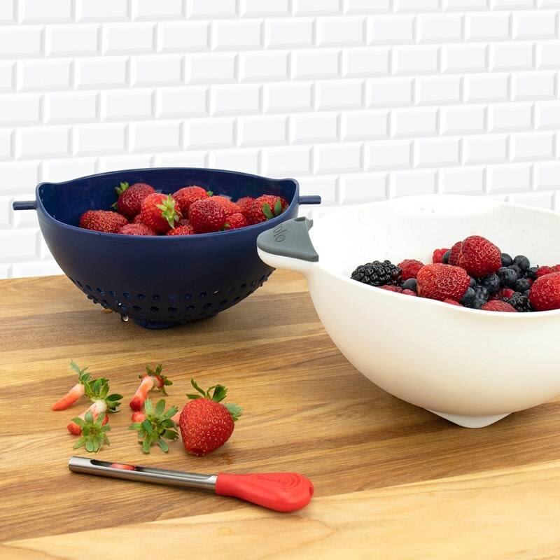 Deep indigo colander and white bowl filled with fresh berries on wooden counter in kitchenware setting