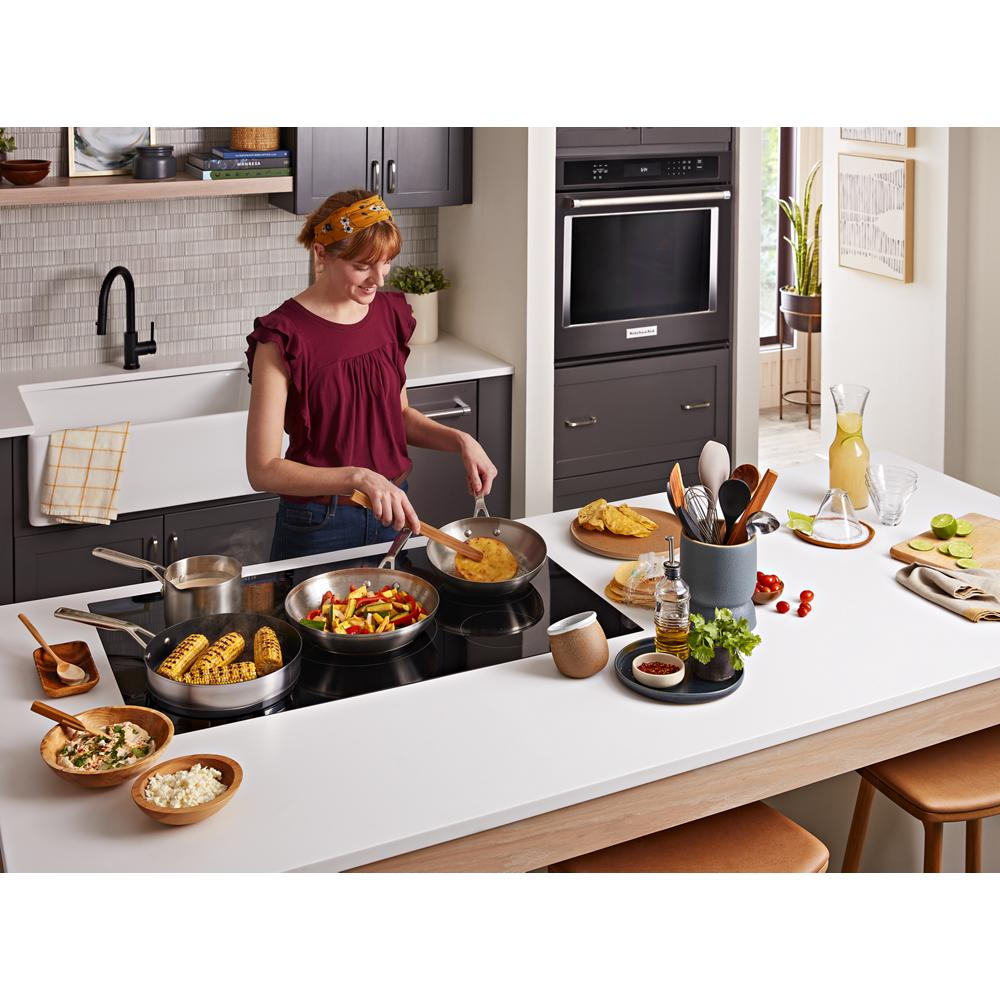 Modern kitchen scene with woman cooking on black 36-inch sensor induction cooktop with five burners