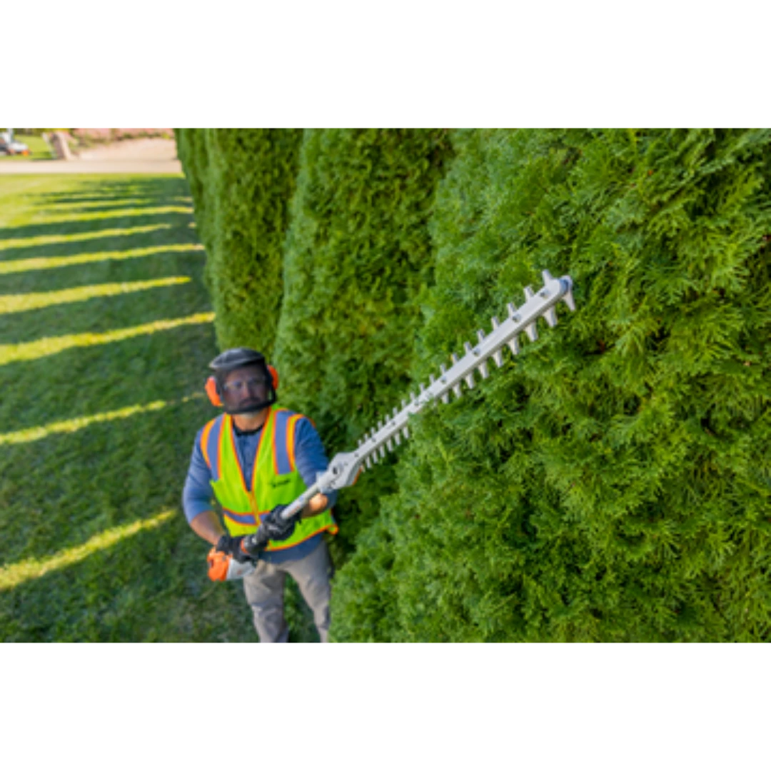 Person wearing safety gear trimming tall green hedge with extended-reach battery hedge trimmer for home improvement tasks