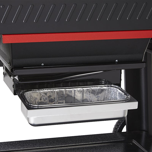 Close-up of the grease tray and drip pan of a black and red pellet grill, designed for clean and convenient outdoor grilling maintenance.