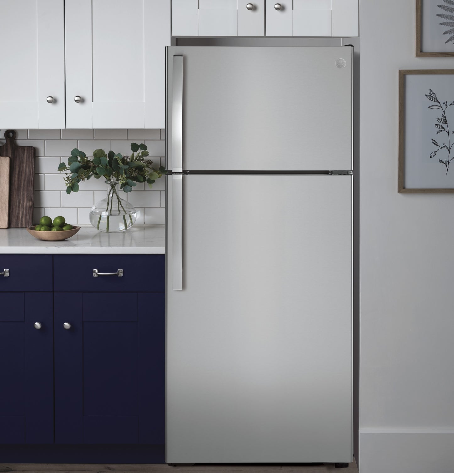 Stainless steel top-freezer refrigerator standing next to navy lower cabinets and white upper kitchen cabinetry in modern kitchen setting