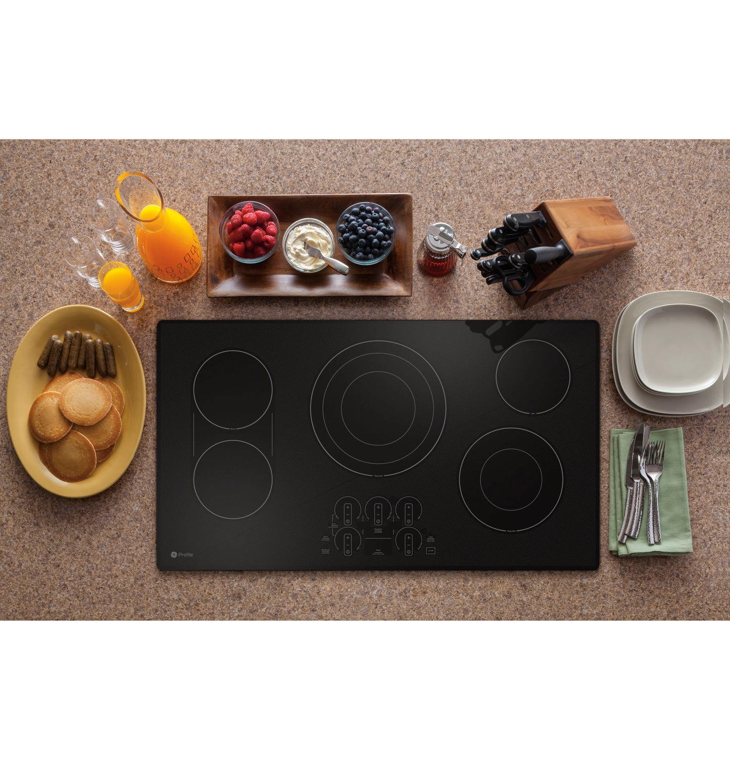 Black glass electric cooktop with touch controls surrounded by breakfast items and dining utensils on countertop
