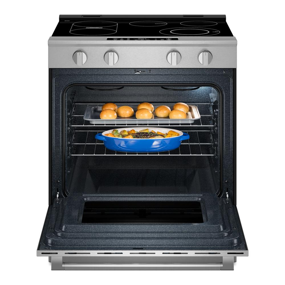 Open stainless steel slide-in electric range with baked rolls and roasted vegetables inside oven cavity in kitchen appliance setting