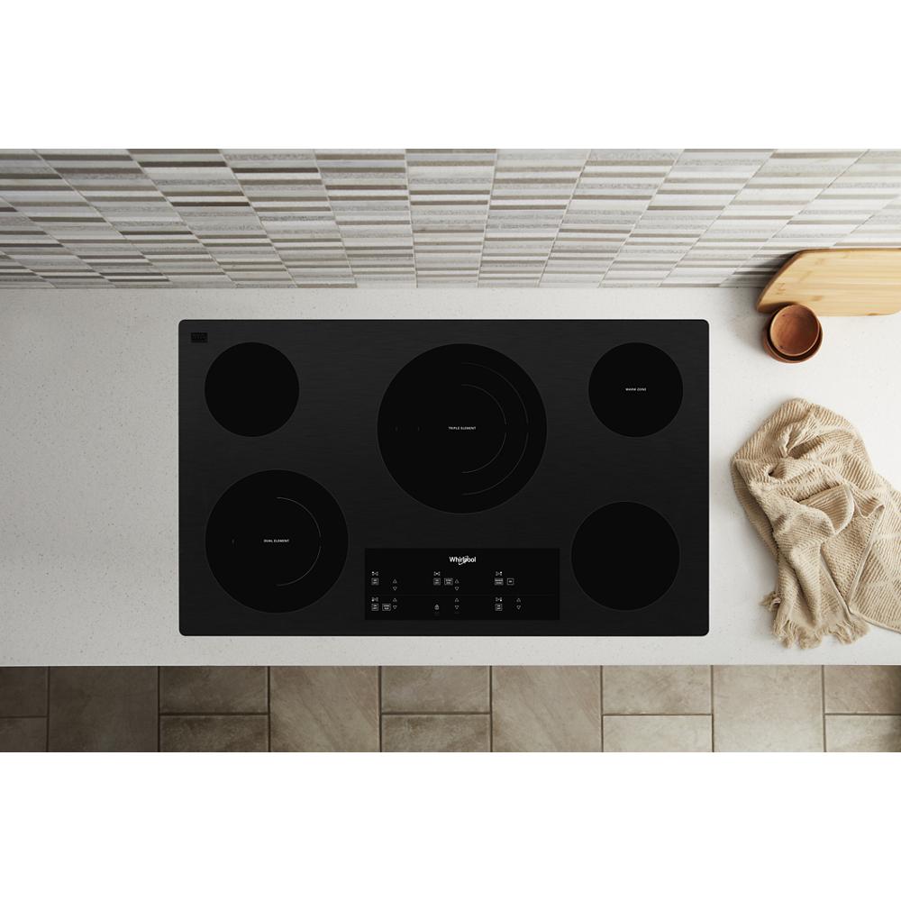 Top view of black electric cooktop with four burners and digital control panel on kitchen countertop with tile backsplash