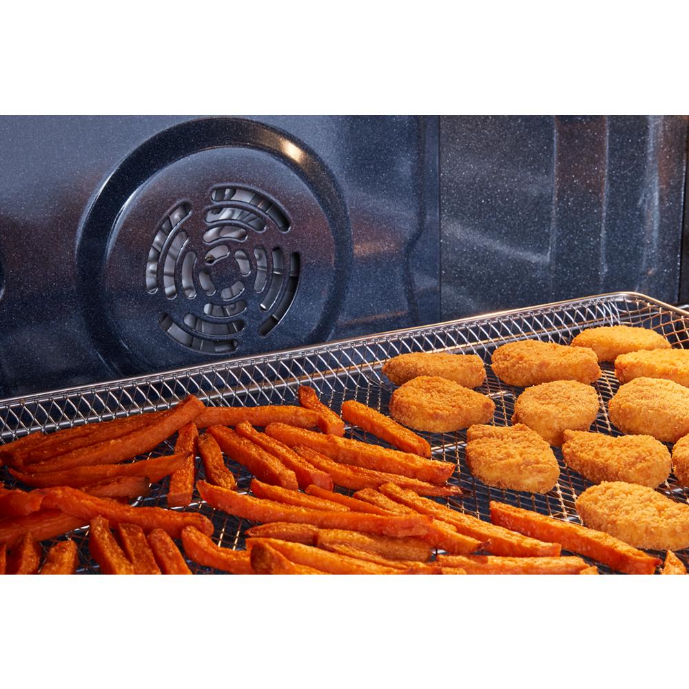Close-up of electric oven interior air frying sweet potato fries and breaded chicken nuggets on wire rack