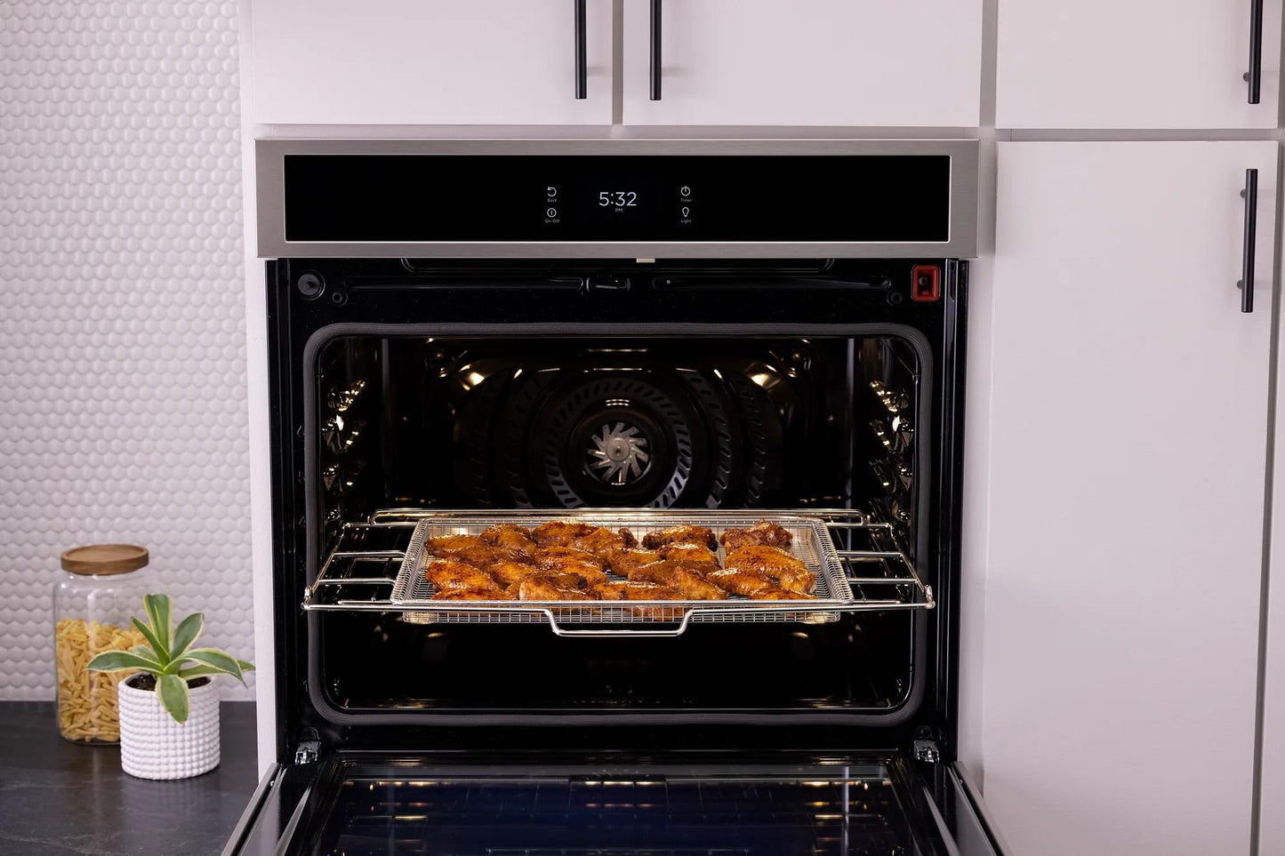 Open double electric wall oven with tray of roasted chicken inside in modern kitchen setting
