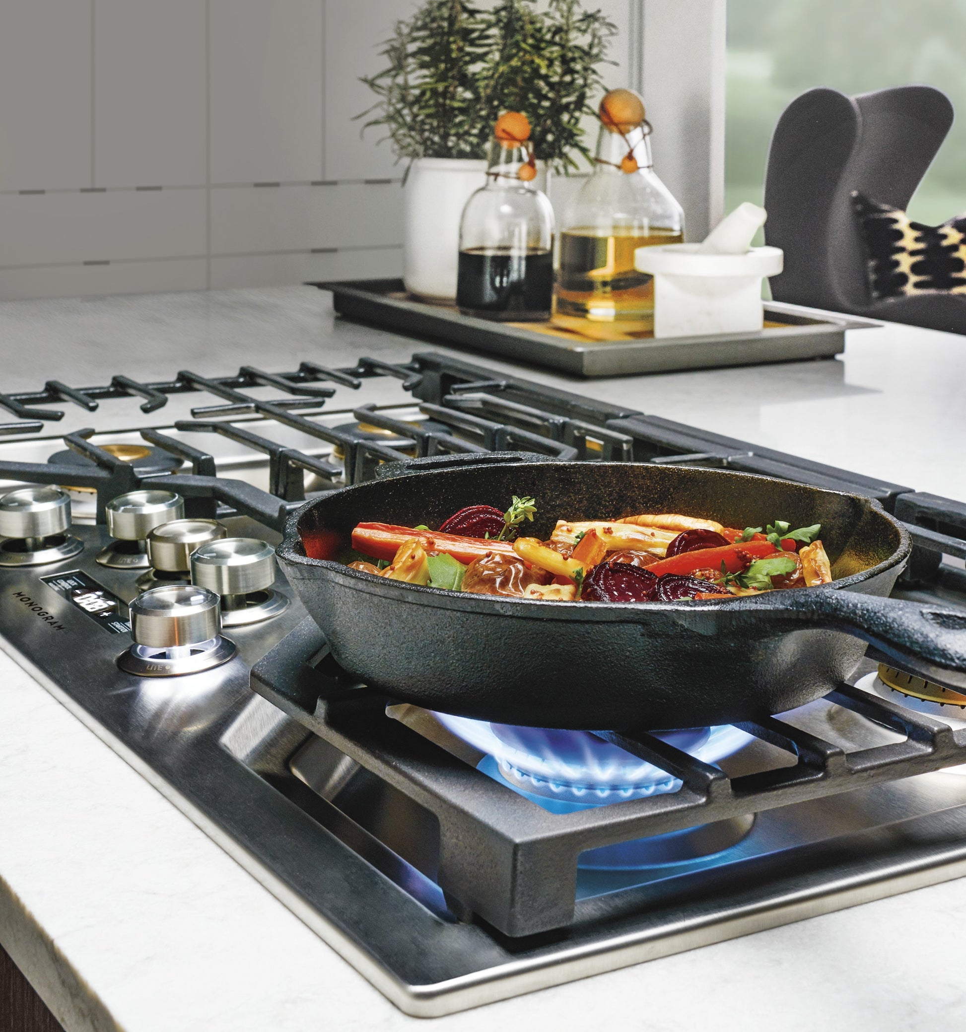 Cast iron skillet cooking vegetables on burner with blue flame on stainless steel cooktop in modern kitchen setting