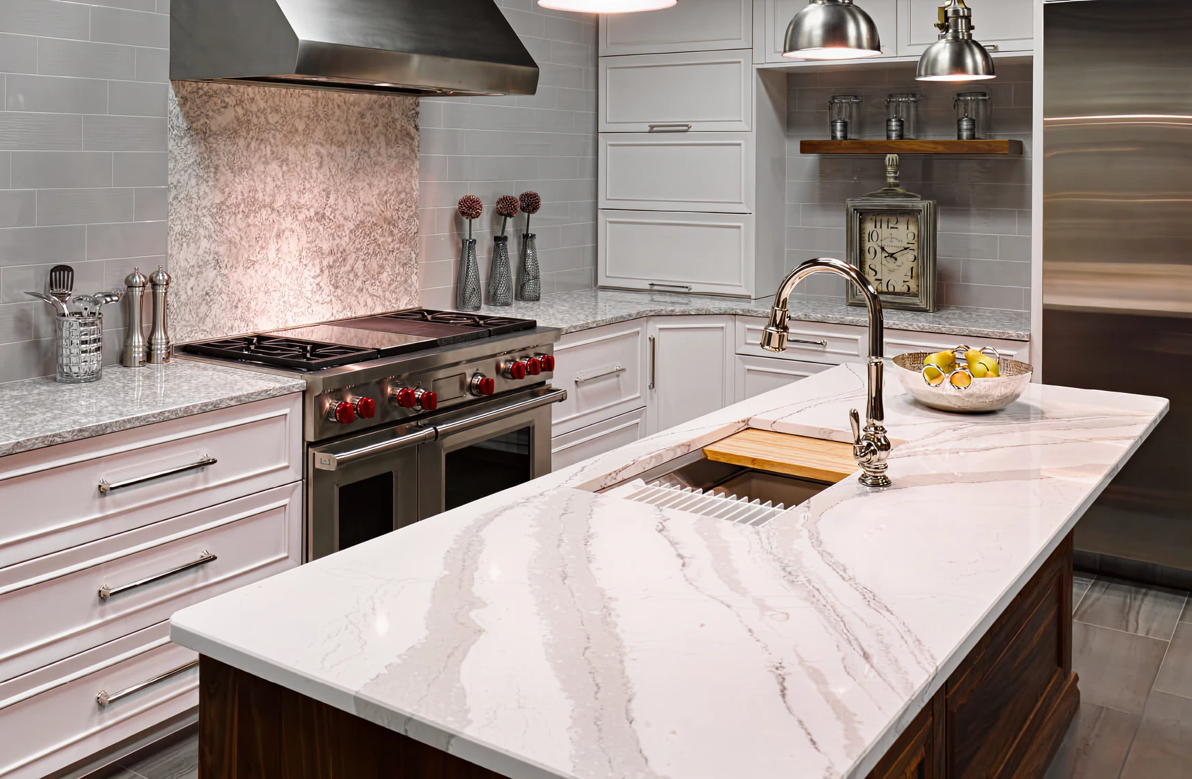 Bright kitchen with white cabinetry, marble countertops, stainless steel appliances, and a large island featuring a modern faucet and decorative bowl of fruit.