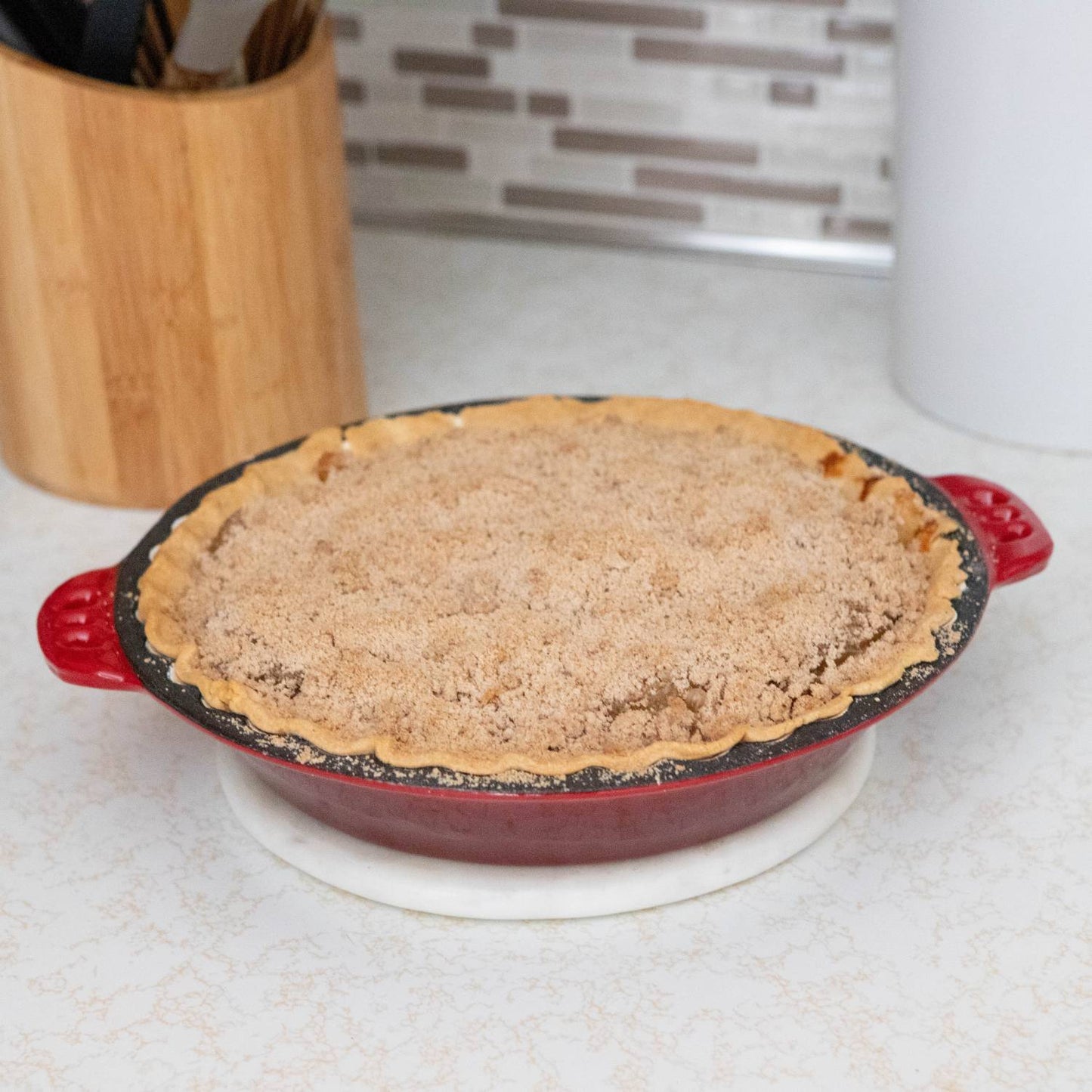 Baked pie with crumb topping in red cast iron pan with crimped edges on white kitchen countertop under $50 collection