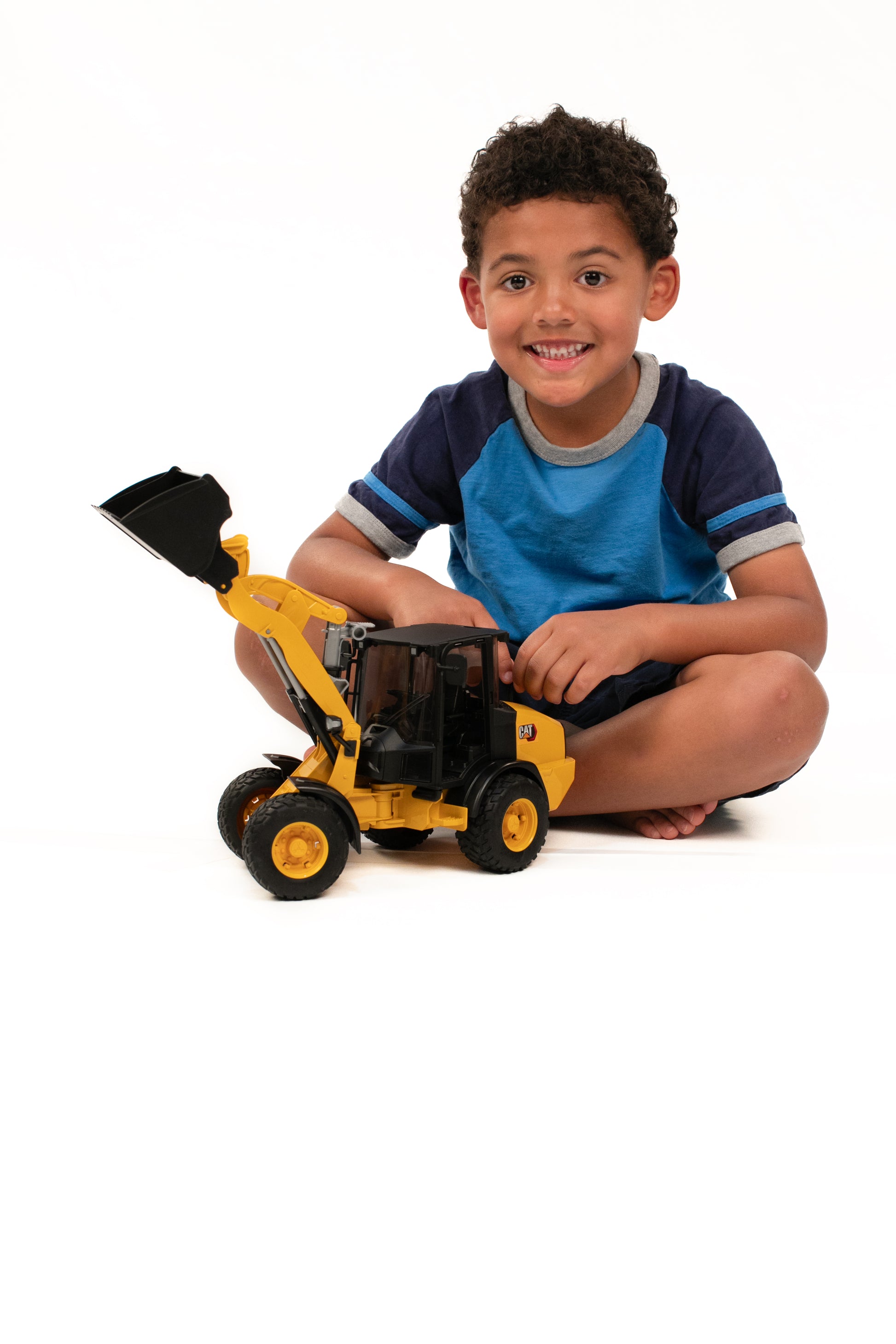 Young child playing with yellow Bruder CAT wheel loader toy model in tools and home improvement setting