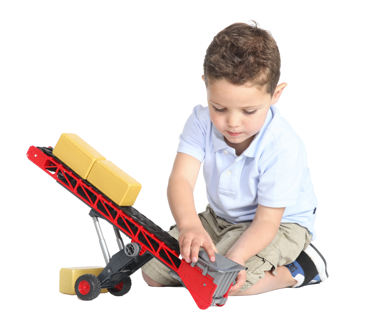 Young child playing with a red and black toy conveyor belt carrying yellow bales in Bruder Toys collection