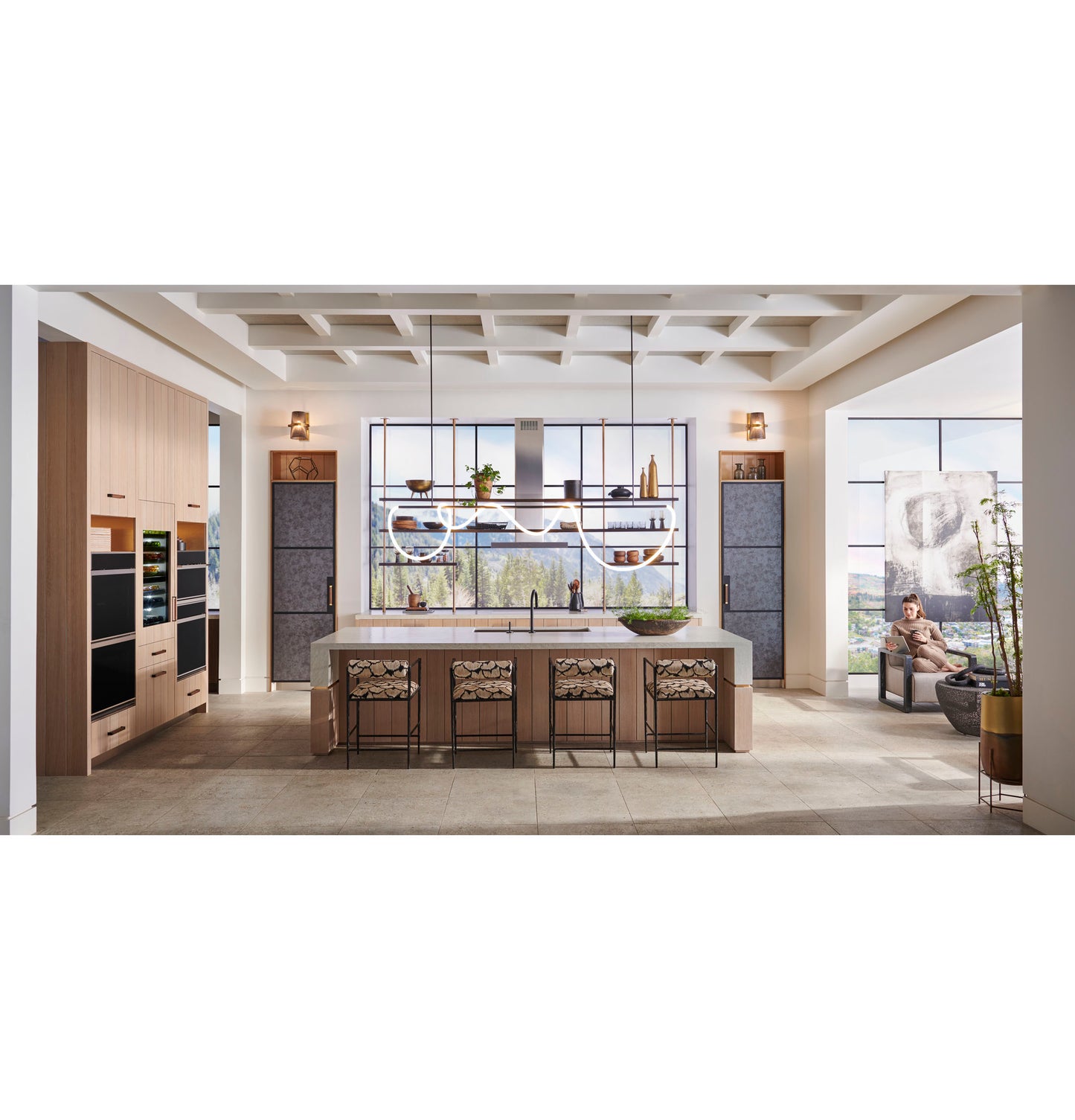 Spacious kitchen with wood cabinets, Monogram double wall ovens, large island with patterned stools, and panoramic window views