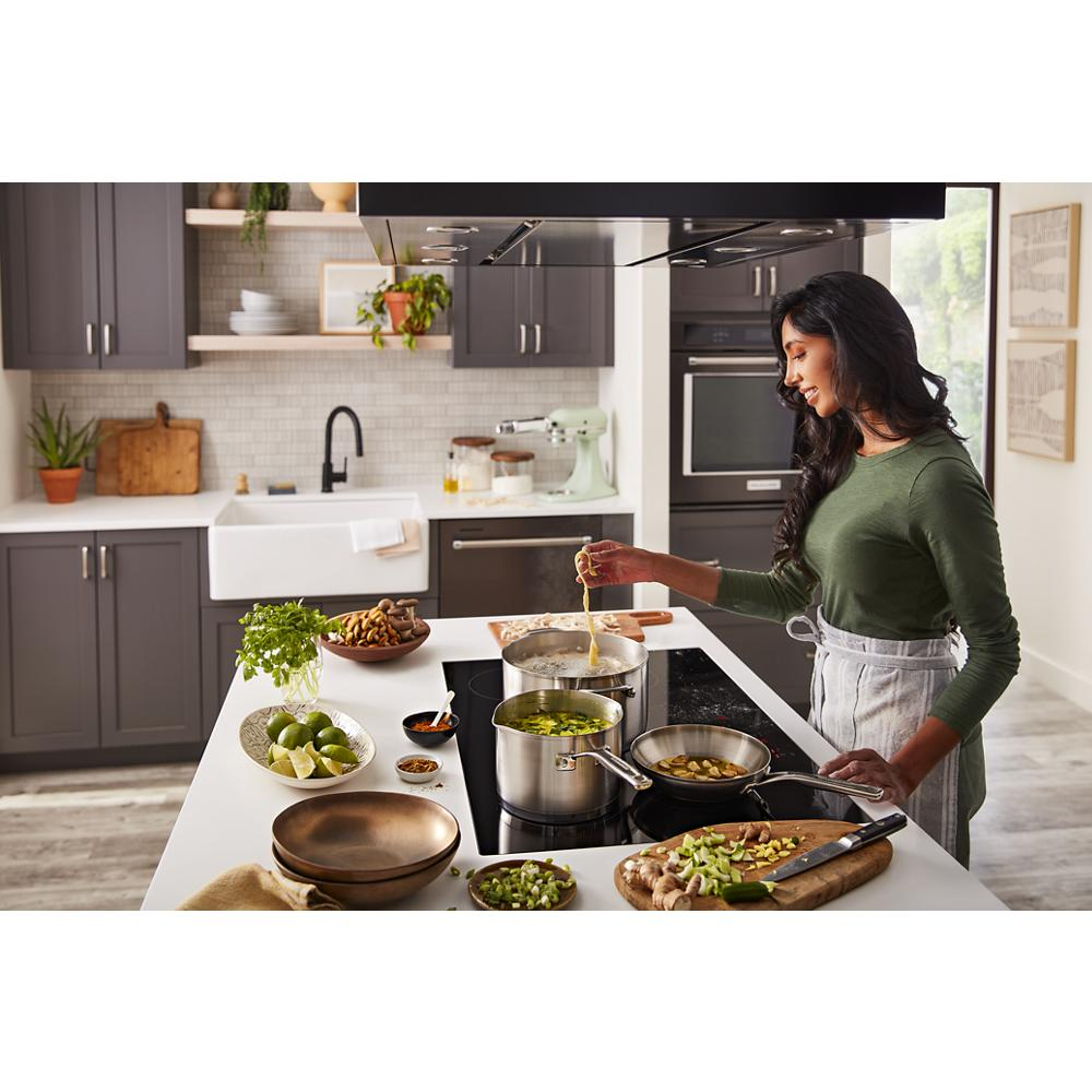Woman cooking in modern kitchen with gray cabinets using a black 30-inch induction cooktop with five elements