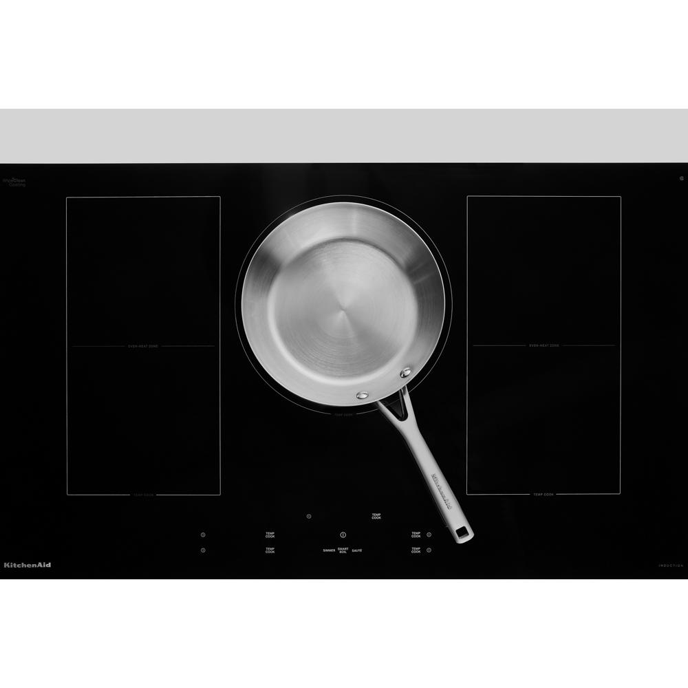 Black glass induction cooktop with five cooking zones and a stainless steel frying pan centered on one burner