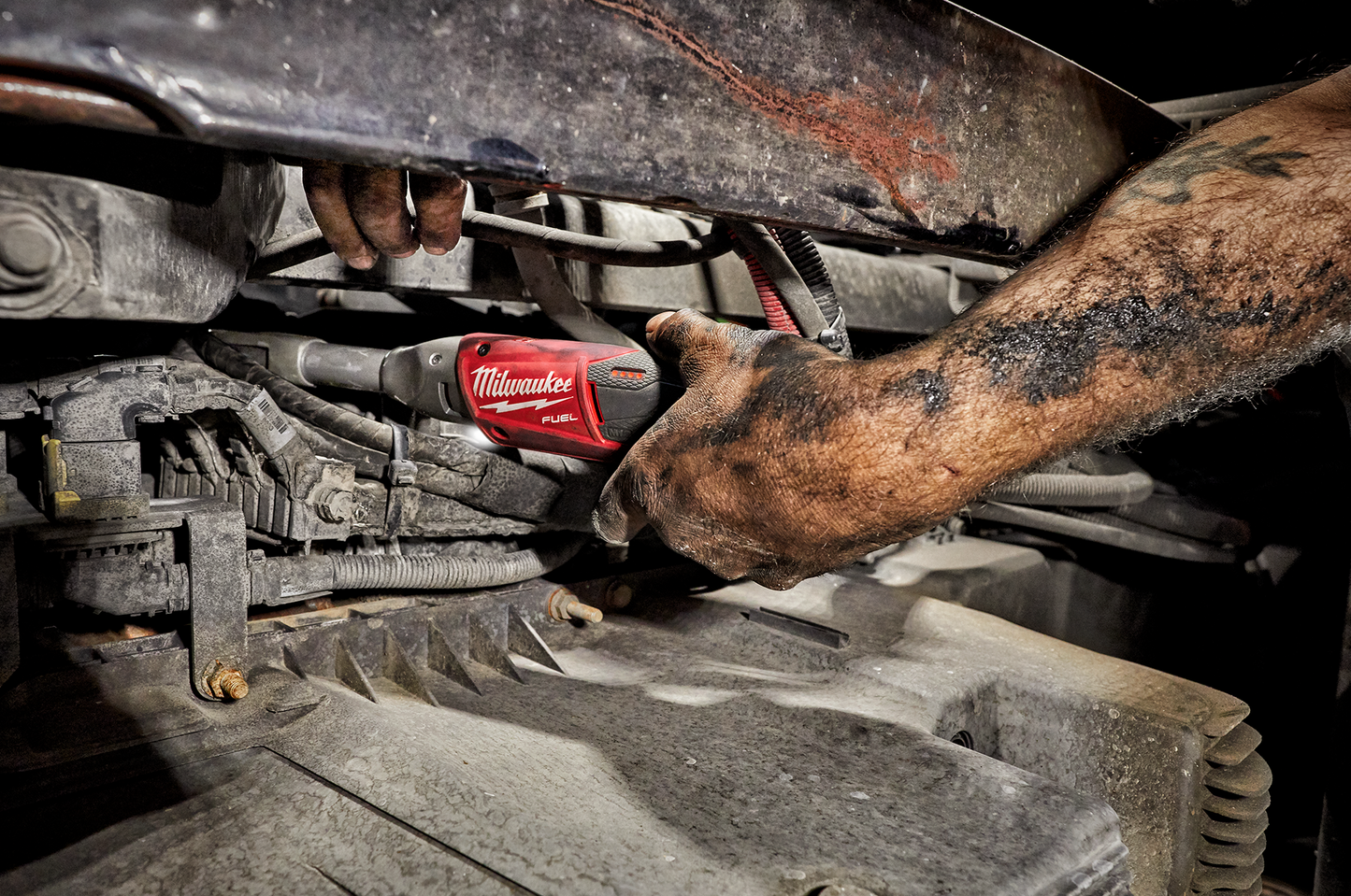 Dirty hands using a red Milwaukee M12 FUEL extended reach ratchet for automotive home improvement task