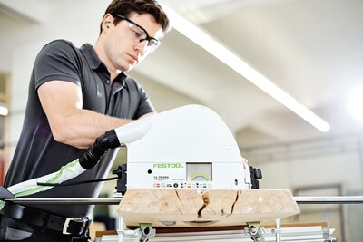 Worker operating a Festool plunge cut saw on thick wood piece in a bright workshop for home improvement tools collection