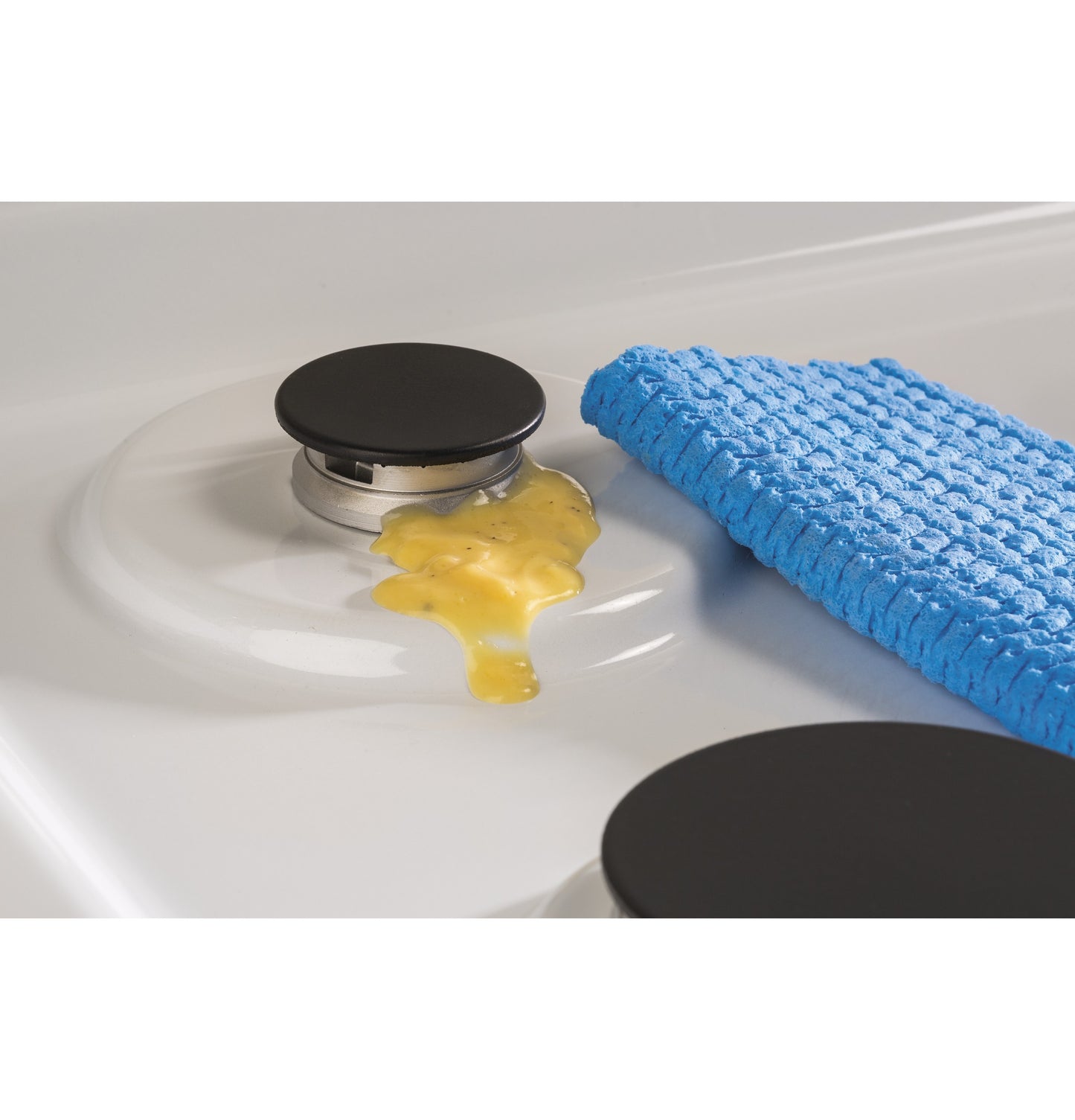 Close-up of white gas cooktop burner with spilled egg and blue textured cleaning cloth nearby in kitchenware collection