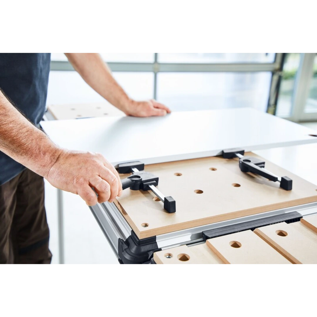 Pair of black cam-action clamping elements securing wood on perforated board for woodworking tool accessories.