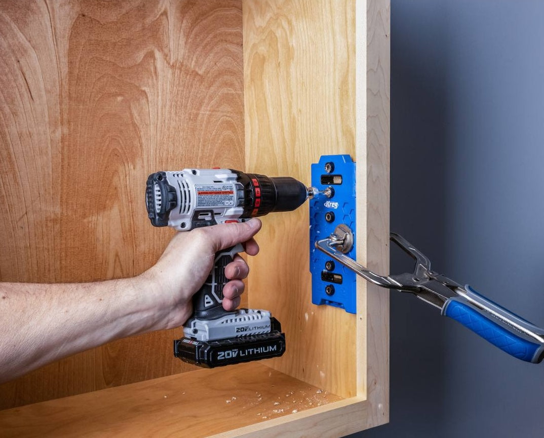Woodworker using blue jig and drill to create precise shelf pin holes in wooden cabinet for home improvement tools