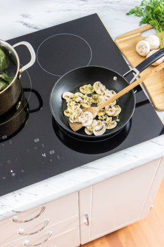 Black European mirror induction cooktop with five cooking zones, showing a pan sautéing mushrooms on a marble countertop