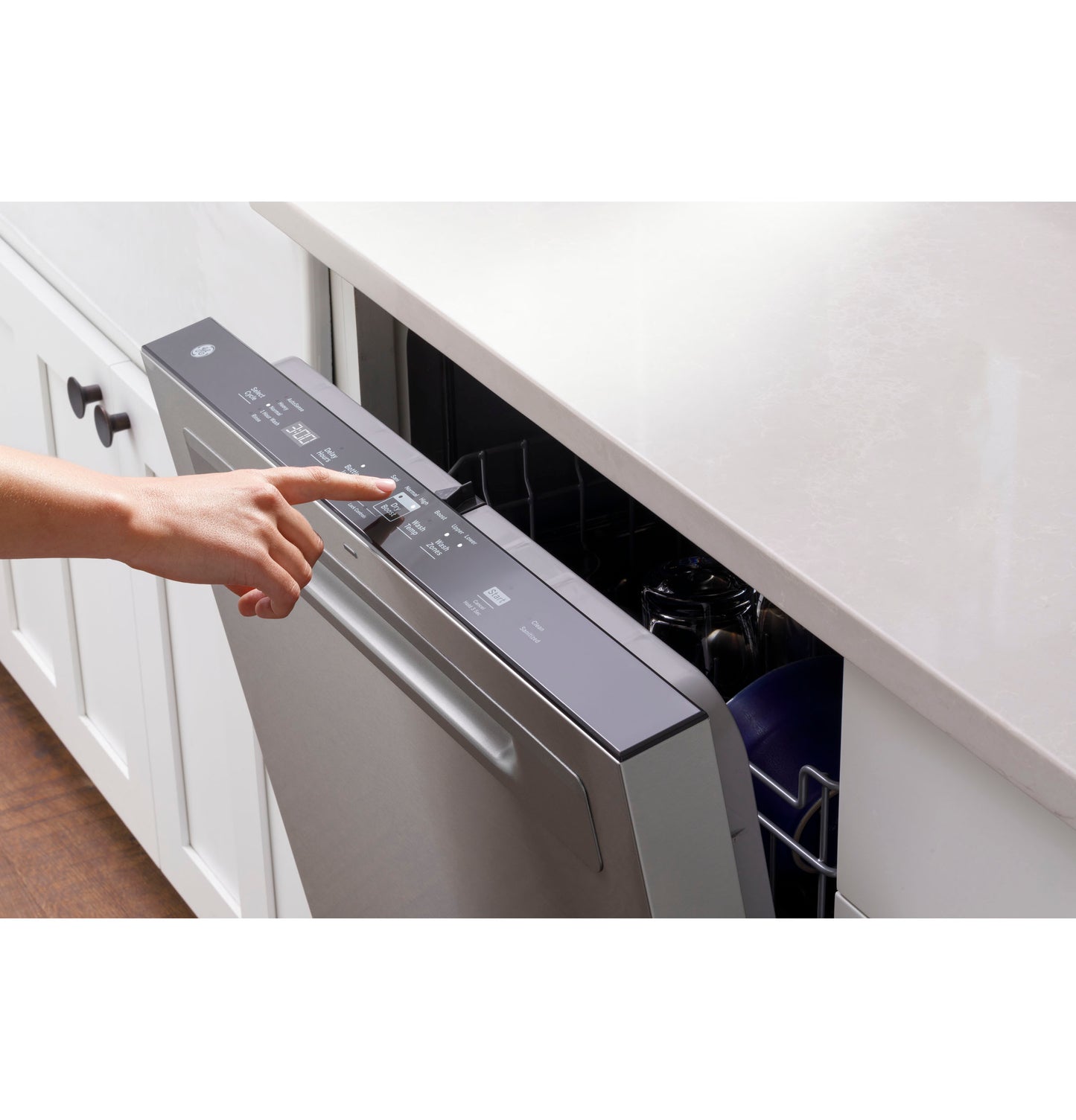 Hand pressing control panel on stainless steel top control dishwasher in modern kitchen appliance setup