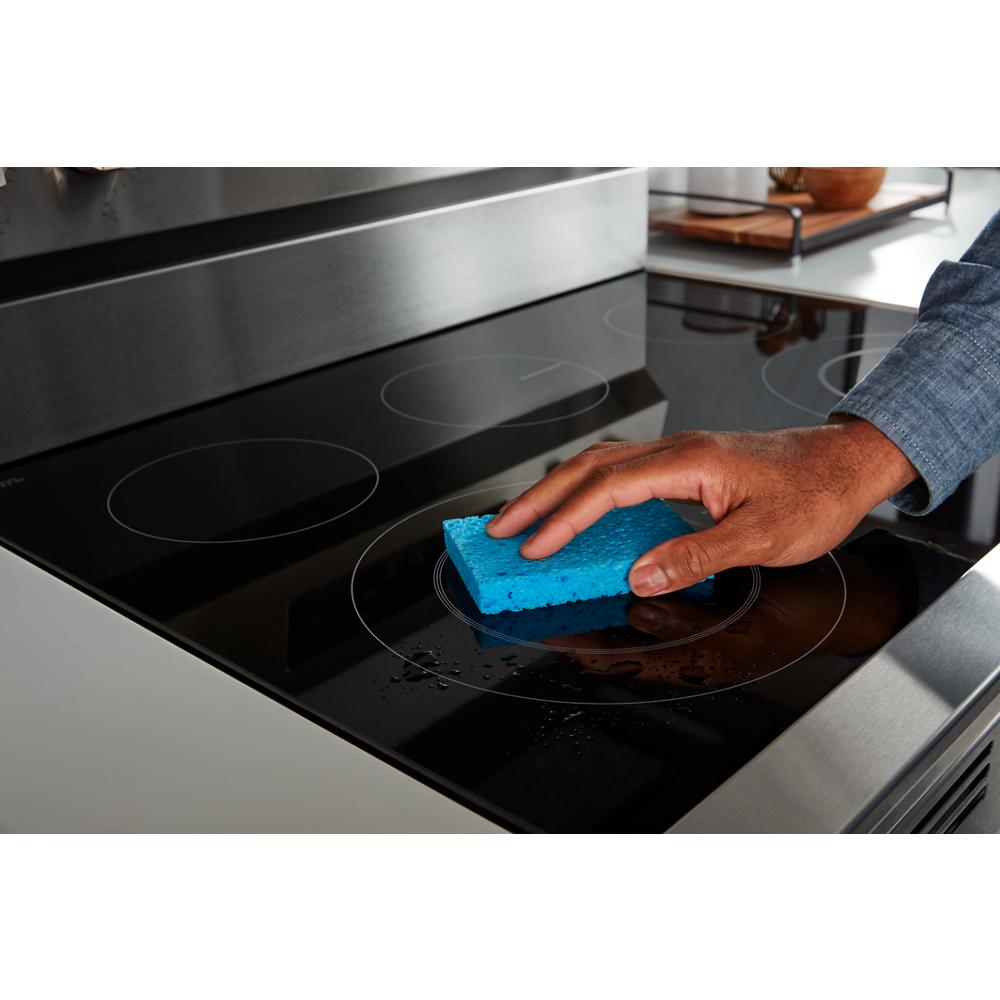 Hand cleaning black ceramic glass cooktop on electric range with blue sponge in modern kitchen setting