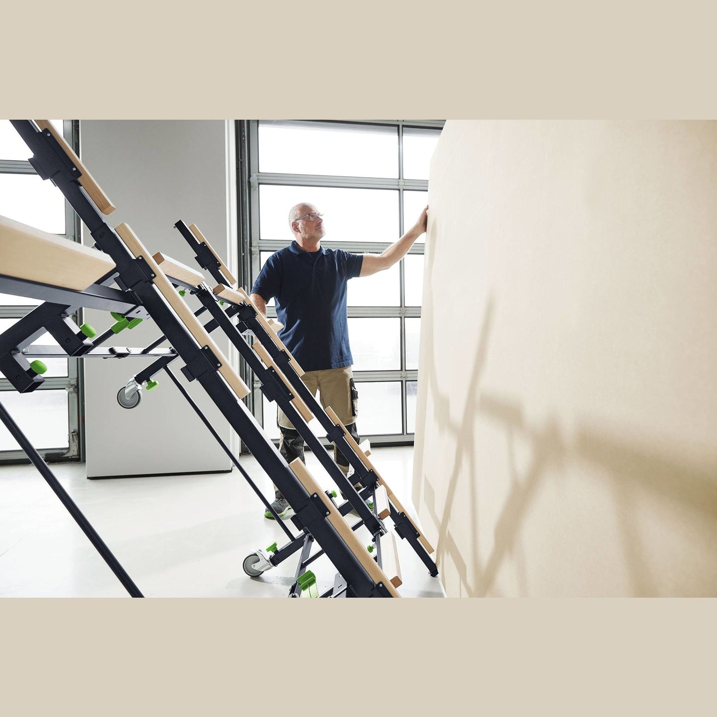 Person loading large sheet onto mobile saw table frame with extendable supports in woodworking tool stand setting