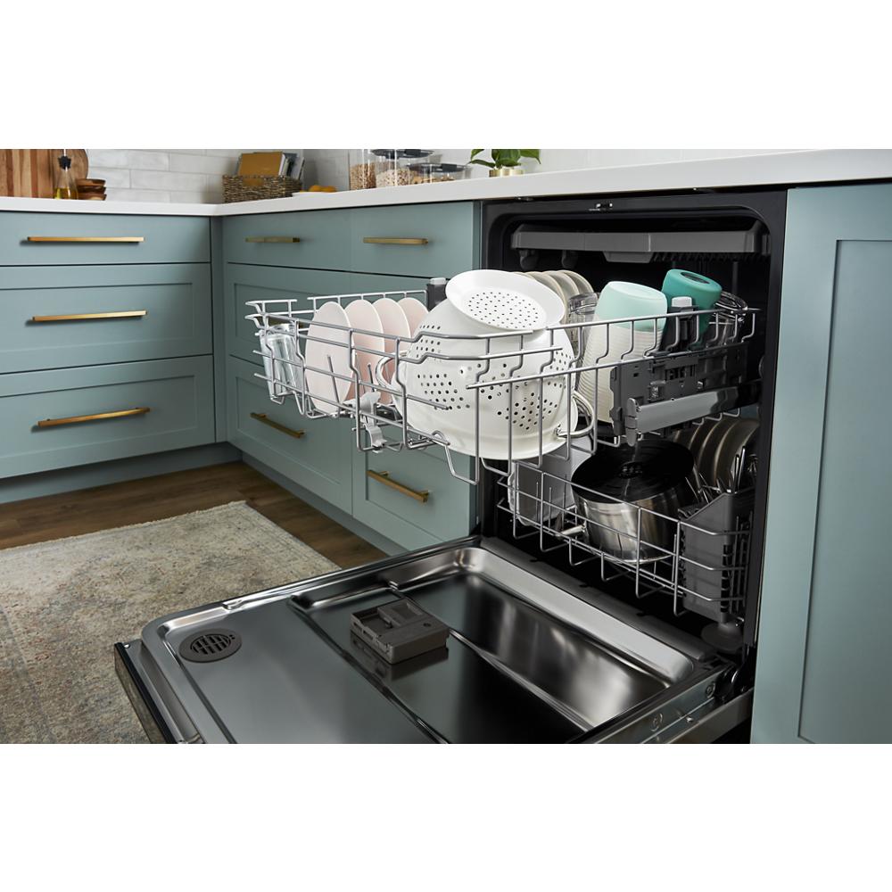 Open dishwasher with third rack loaded with dishes and kitchenware in modern kitchen with blue cabinetry