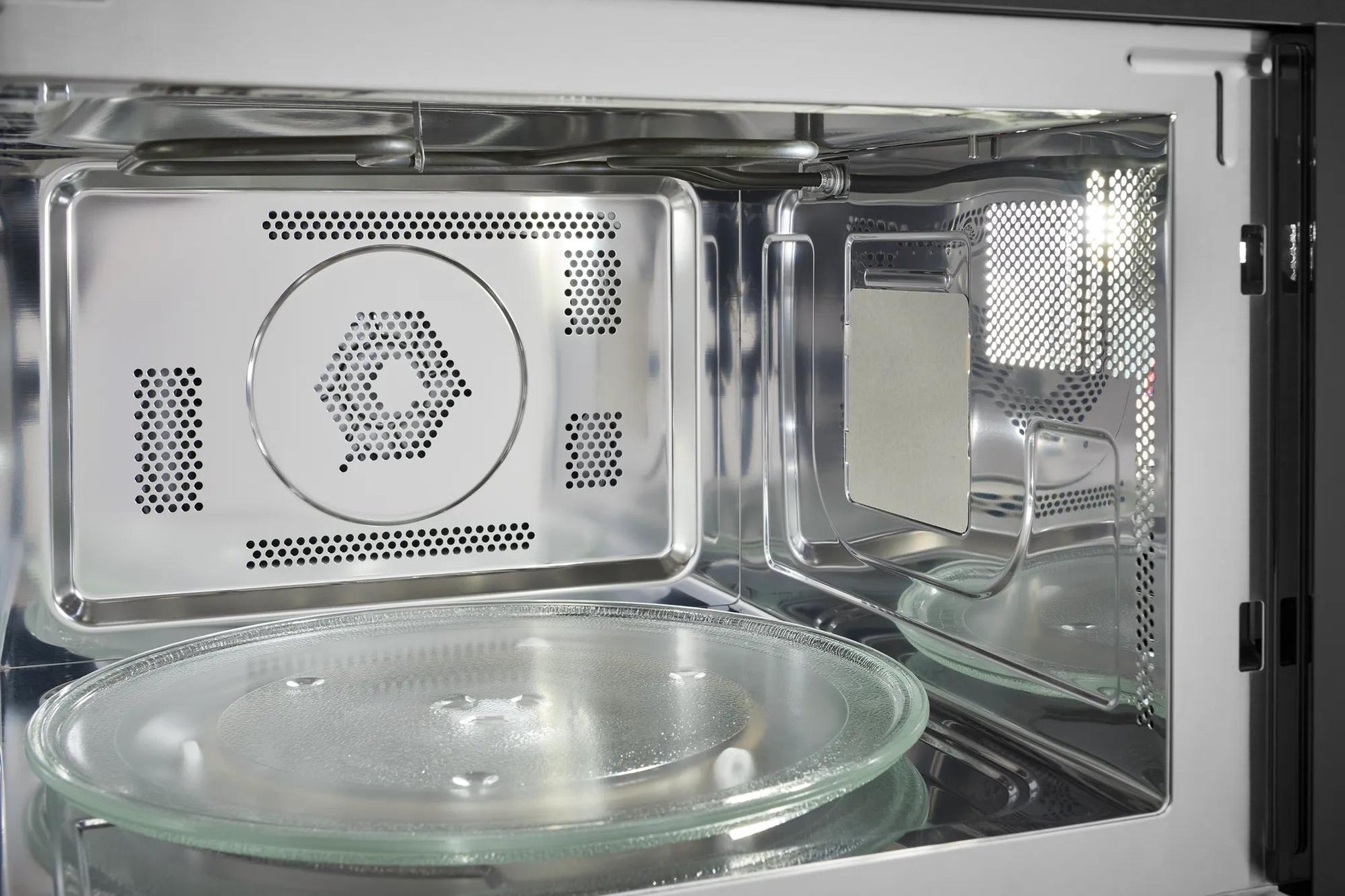 Interior view of a stainless steel built-in microwave oven with glass turntable and ventilation holes visible inside