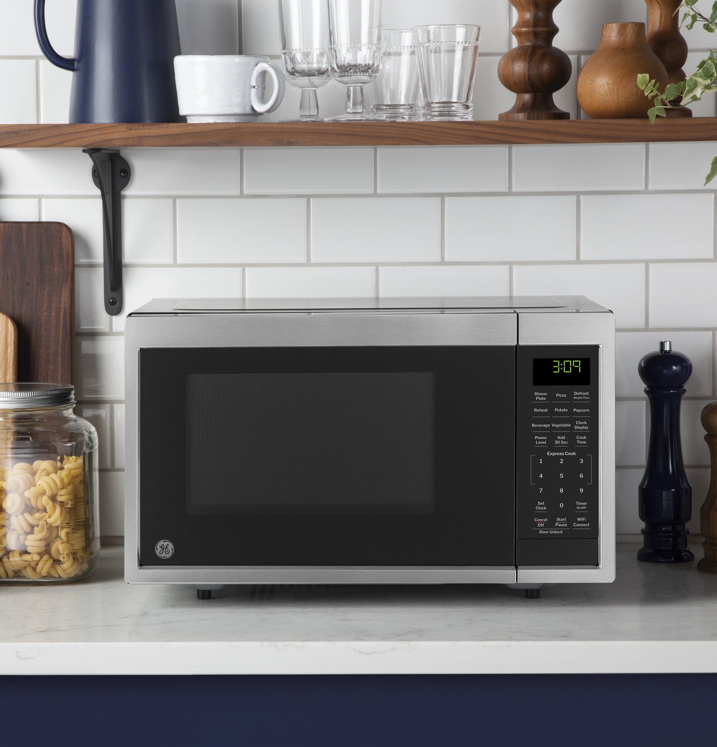 Stainless steel microwave on kitchen counter with digital control panel near pasta jar and countertop decor
