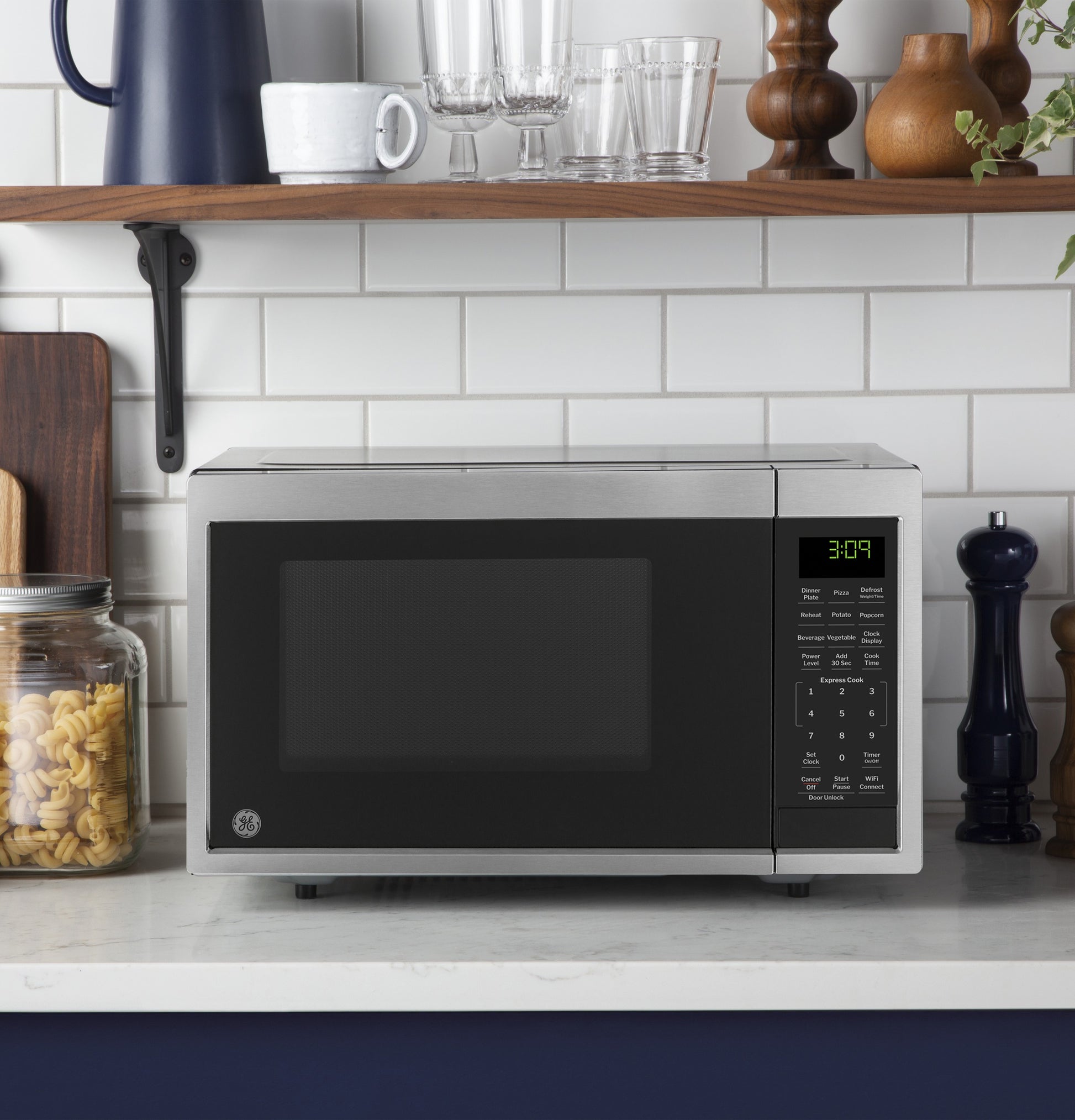 Stainless steel microwave on kitchen counter with digital control panel near pasta jar and countertop decor
