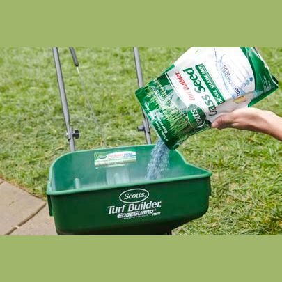 Person pouring grass seed from a Scotts bag into a green lawn spreader for shaded lawn care tasks