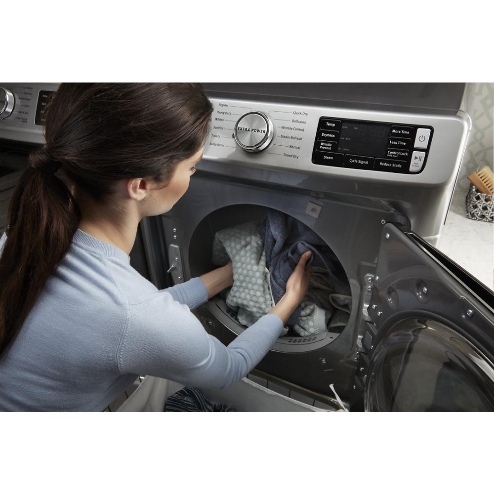 Woman loading clothes into a front load gas dryer with Extra Power control in a modern laundry room setting.