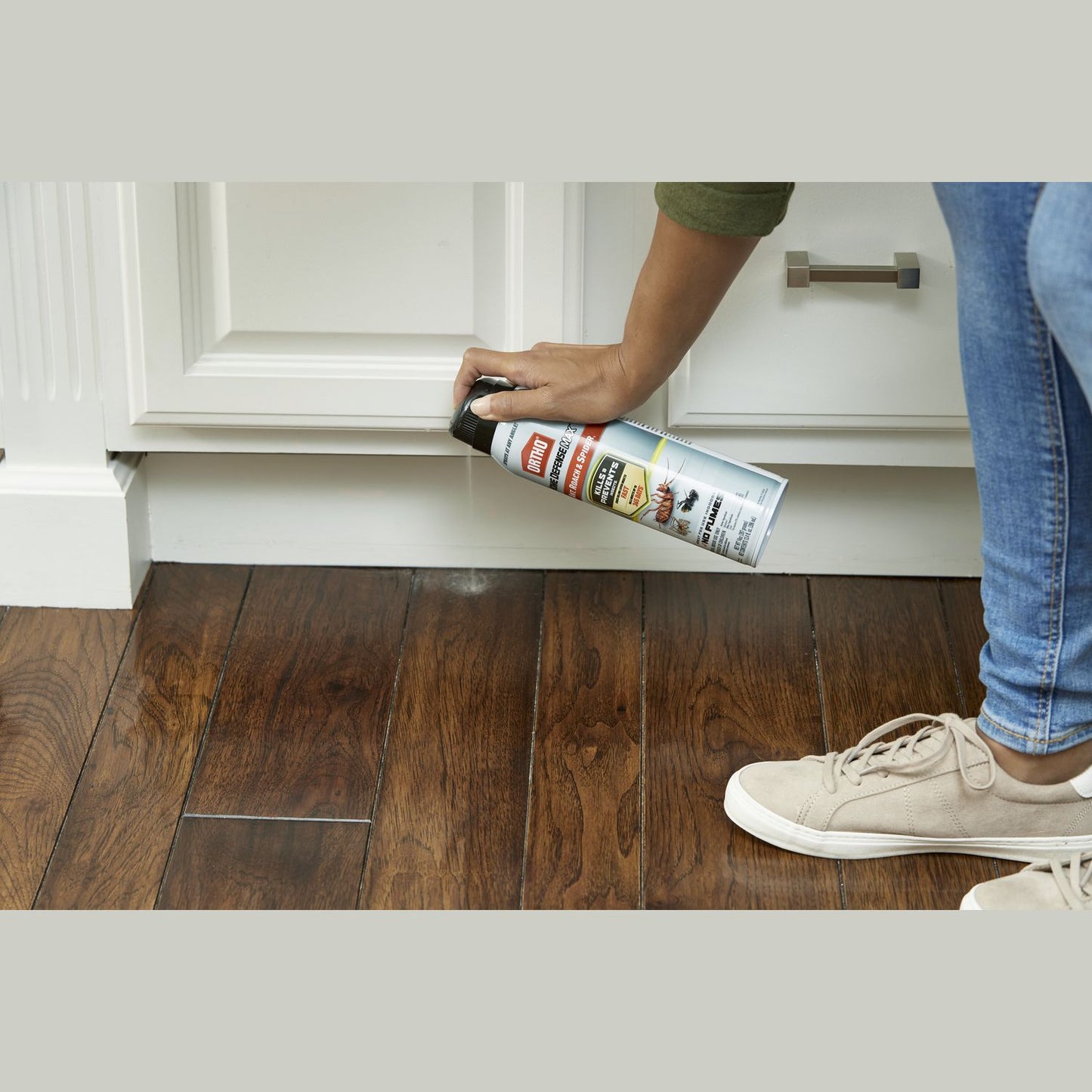 Person using Ortho insecticide spray along baseboard on hardwood floor in insect and pest control category