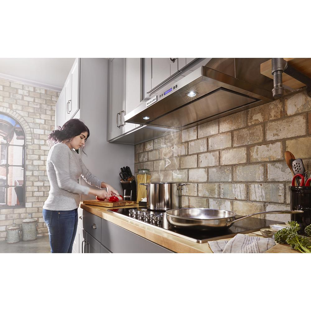 Woman preparing food beside a wooden countertop with a stainless steel electric cooktop and overhead vent in kitchenware setting