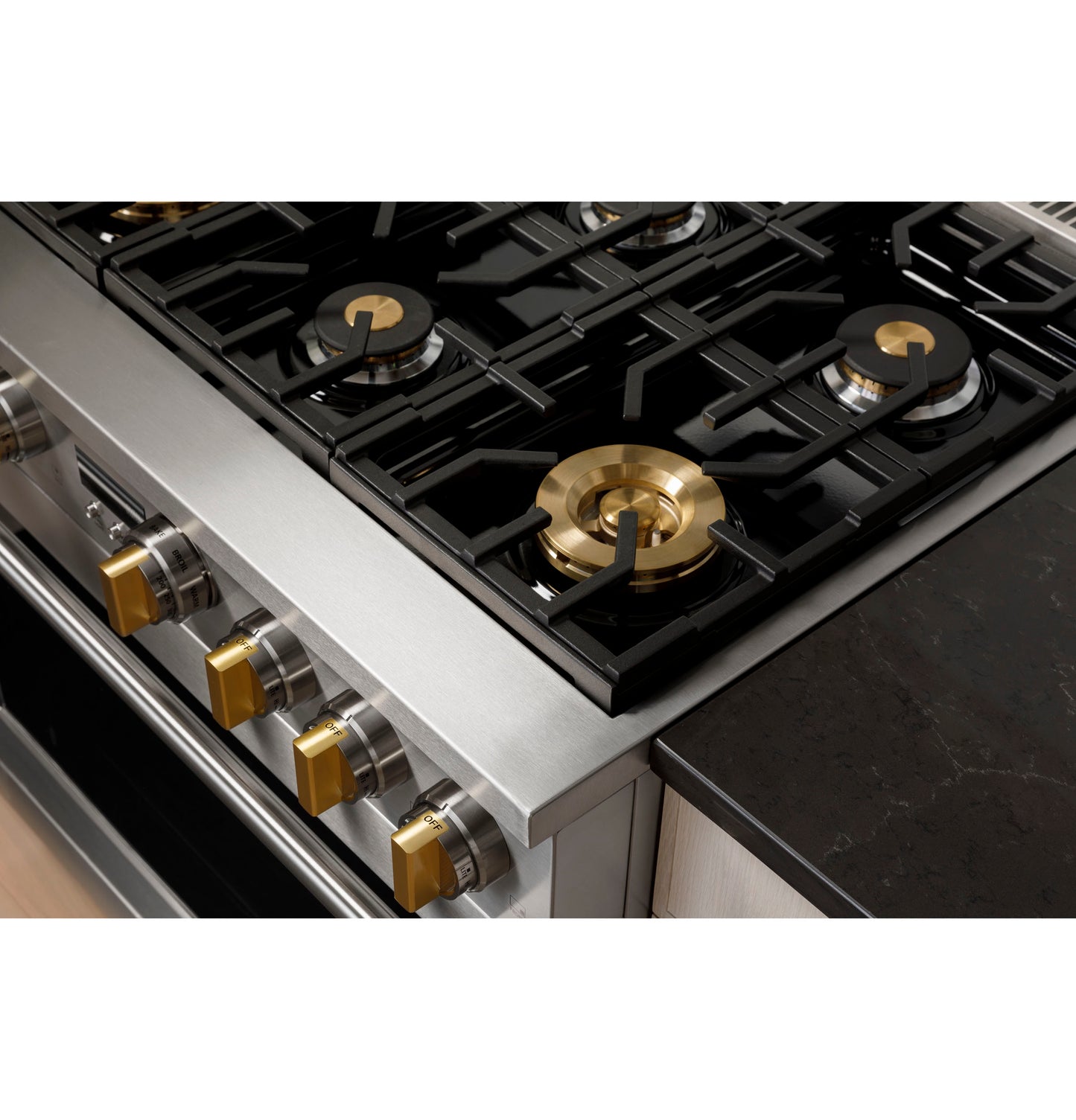 Close-up of stainless steel gas range with brass burners and metallic control knobs next to black countertop in kitchen