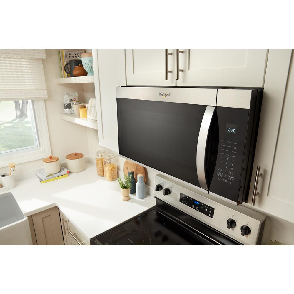 Whirlpool stainless steel microwave mounted above a smooth top electric range in a bright kitchen setting