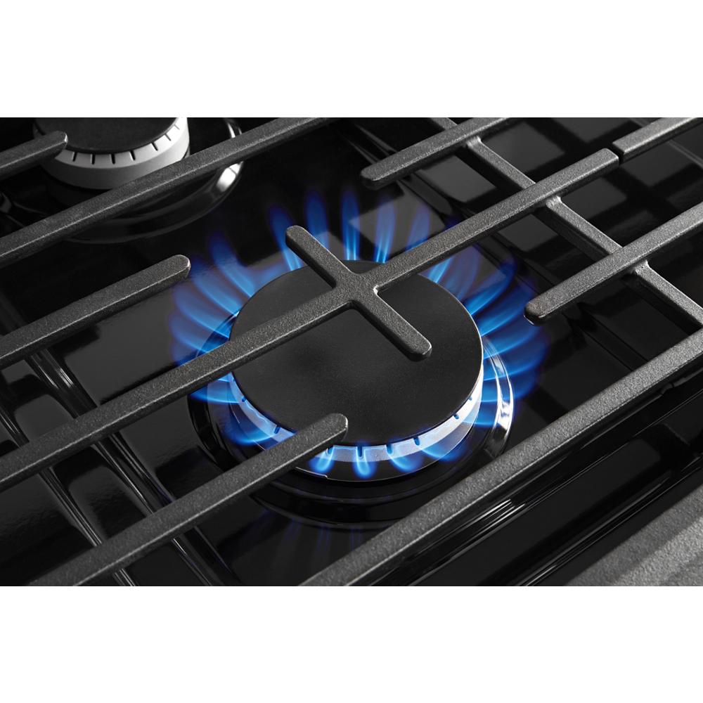 close-up of gas burner with blue flame and cast iron grates on freestanding range for kitchen appliances and home improvement