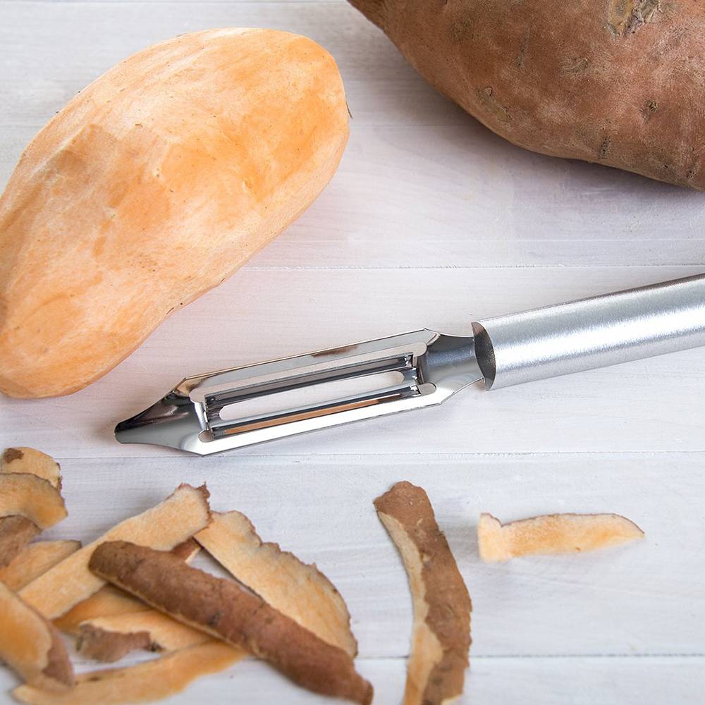 Sleek aluminum-handled peeler with sweet potato and peelings on white wooden surface in kitchen utensils collection under $50