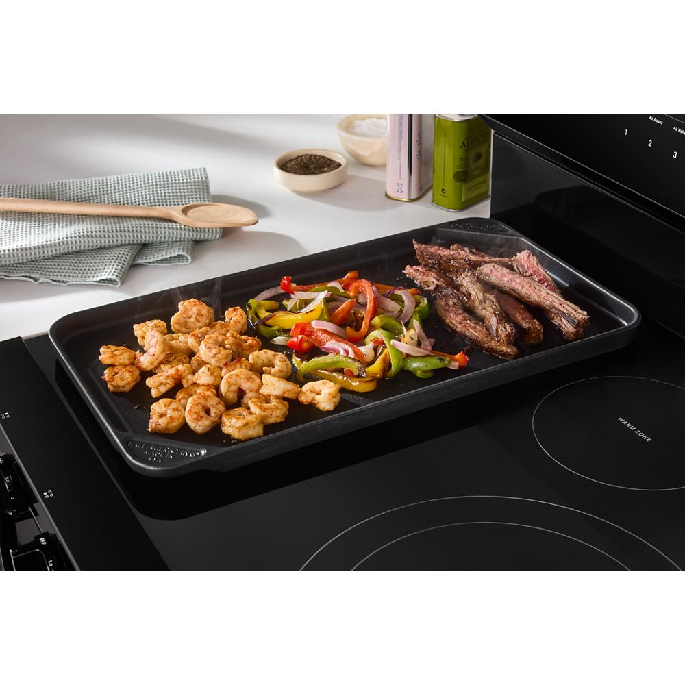 Black electric range with smooth cooktop and griddle cooking shrimp, steak, and mixed bell peppers in kitchenware collection