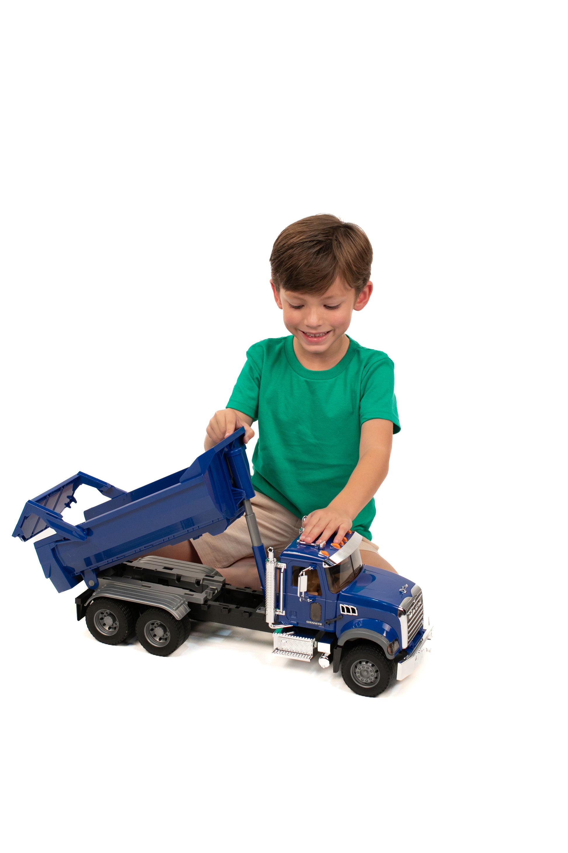 Child playing with blue Bruder 1:16 scale MACK Granite halfpipe dump truck toy on white background