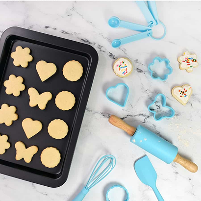 Child-sized blue bakeware set with measuring spoons, rolling pin, spatula, whisk, and cookie cutters for pretend play toys