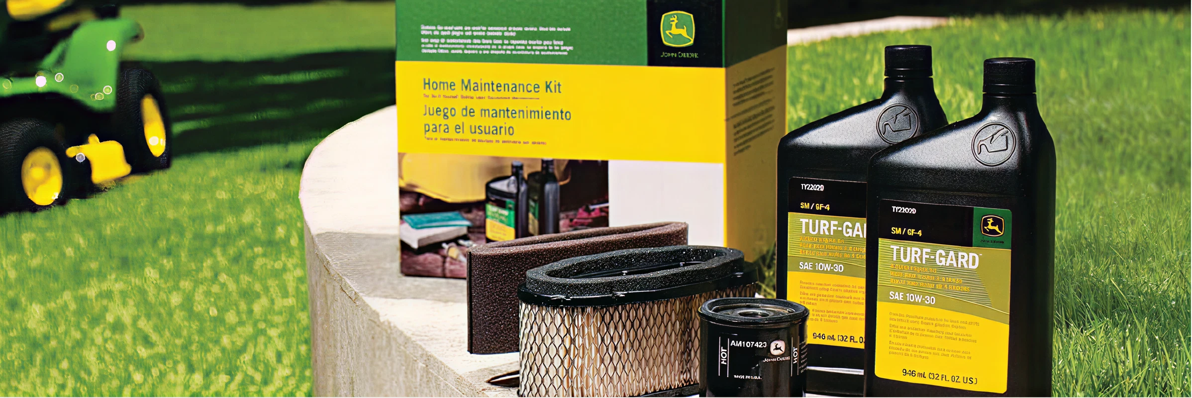 Maintenance kit including oil, filters, and Turf-Gard lubricant containers displayed outdoors on a stone surface beside a green lawn tractor.