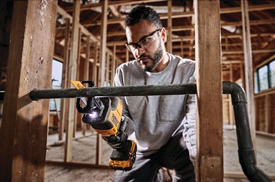 Man wearing safety glasses using DEWALT cordless reciprocating saw to cut metal pipe during home improvement project