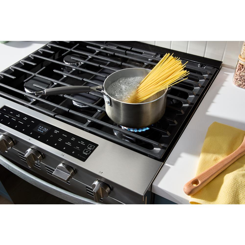 Stainless steel gas range cooktop with digital control panel boiling water with spaghetti on a burner in kitchen setting
