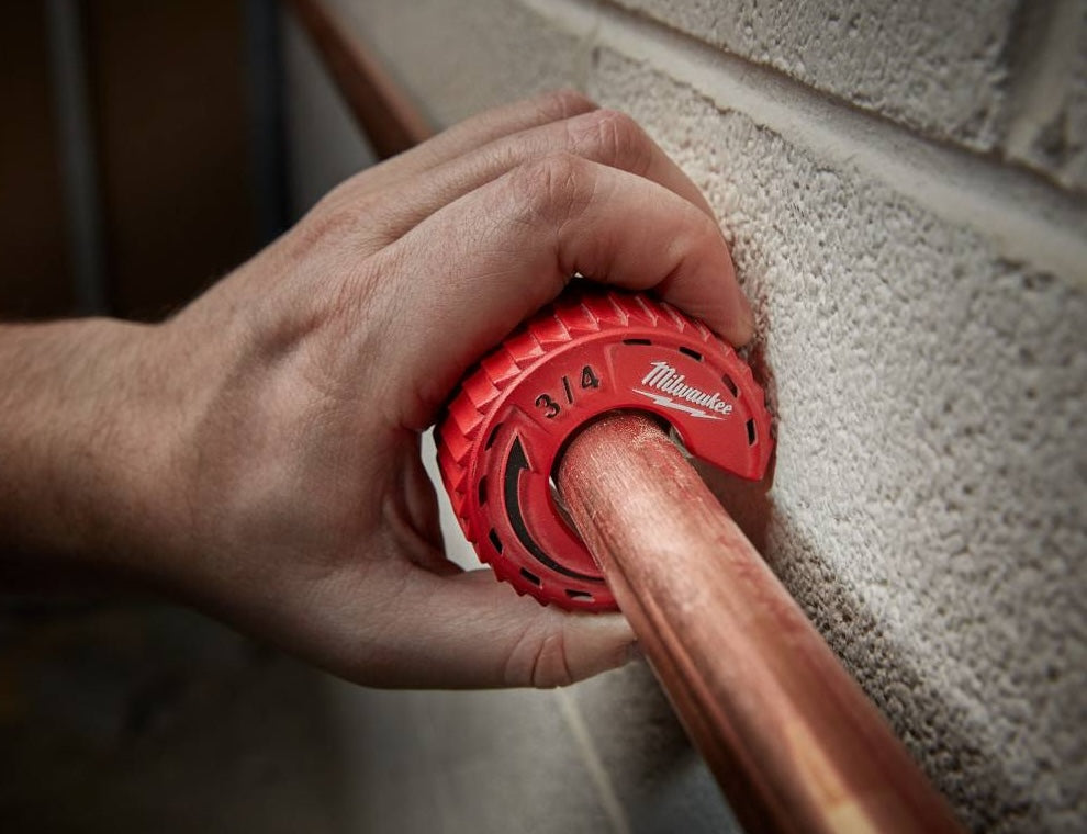 Hand using red Milwaukee 3/4 inch close quarters tubing cutter on copper pipe for home improvement tasks