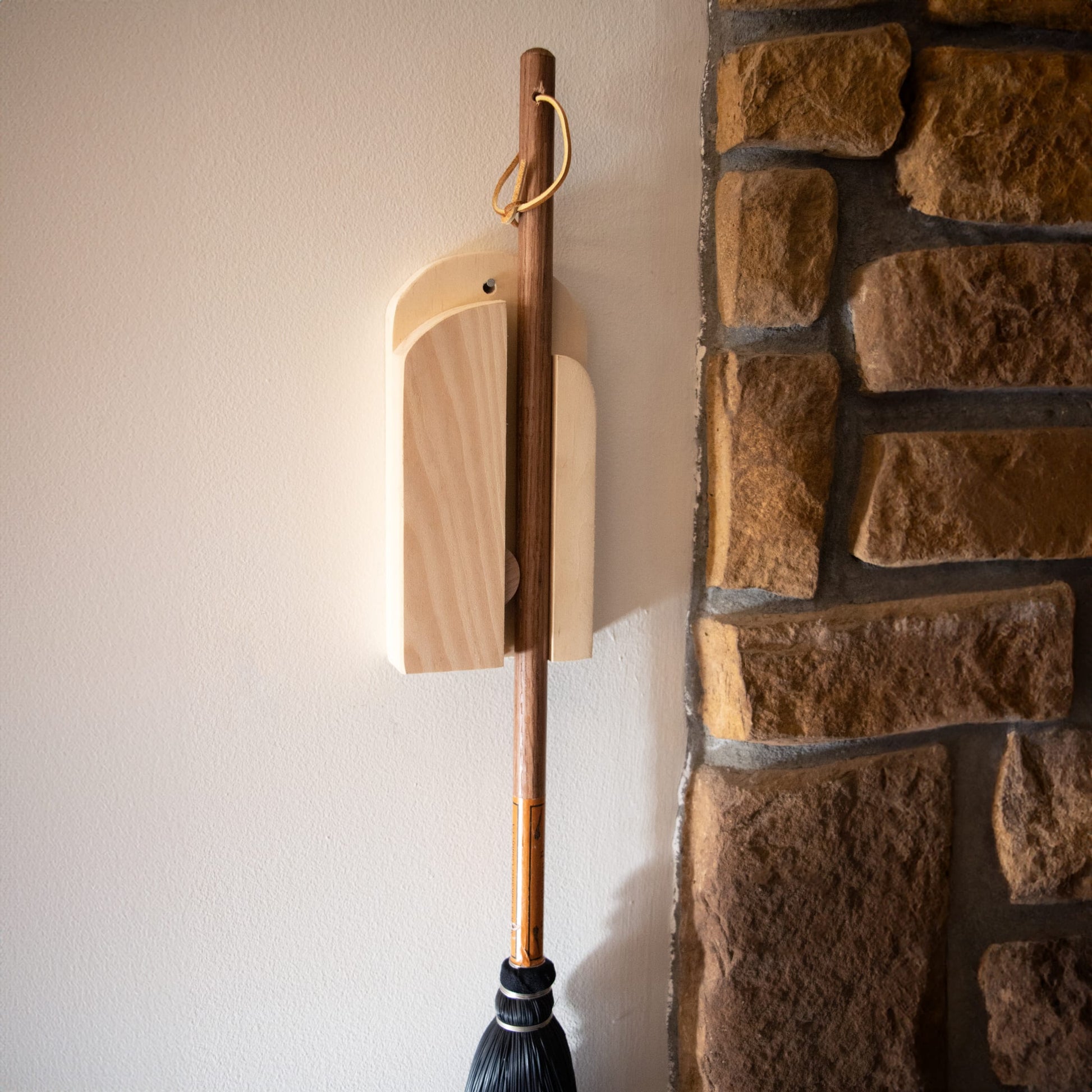 Natural wood broom holder mounted on wall beside rustic stone fireplace in Cleaning Tools and Home Improvement collections under $50