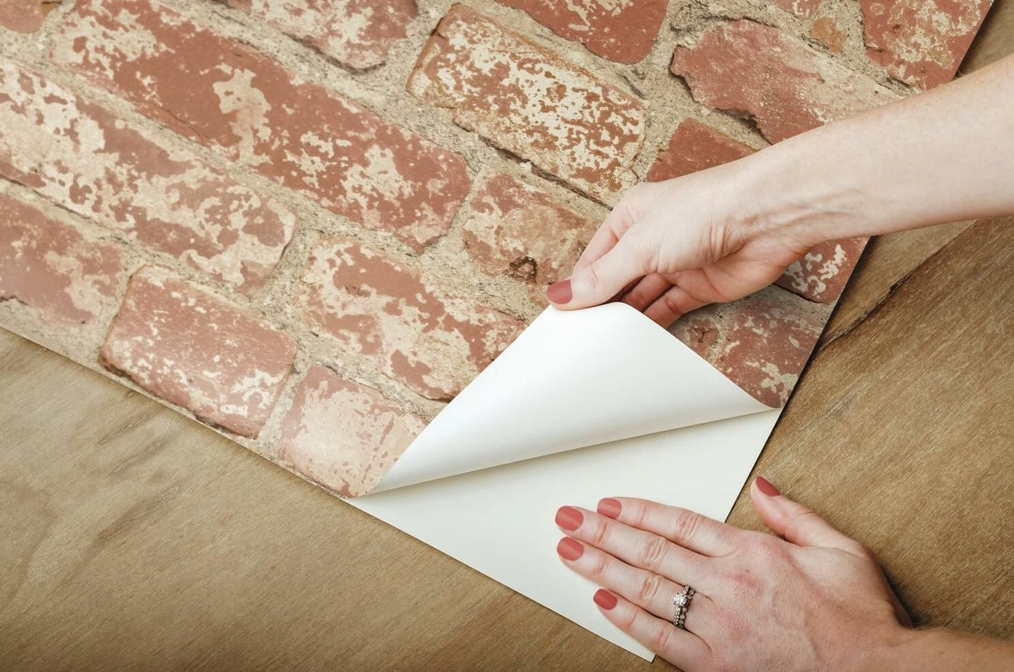 Hands applying stuccoed brick peel and stick wallpaper on wooden surface for easy home improvement projects