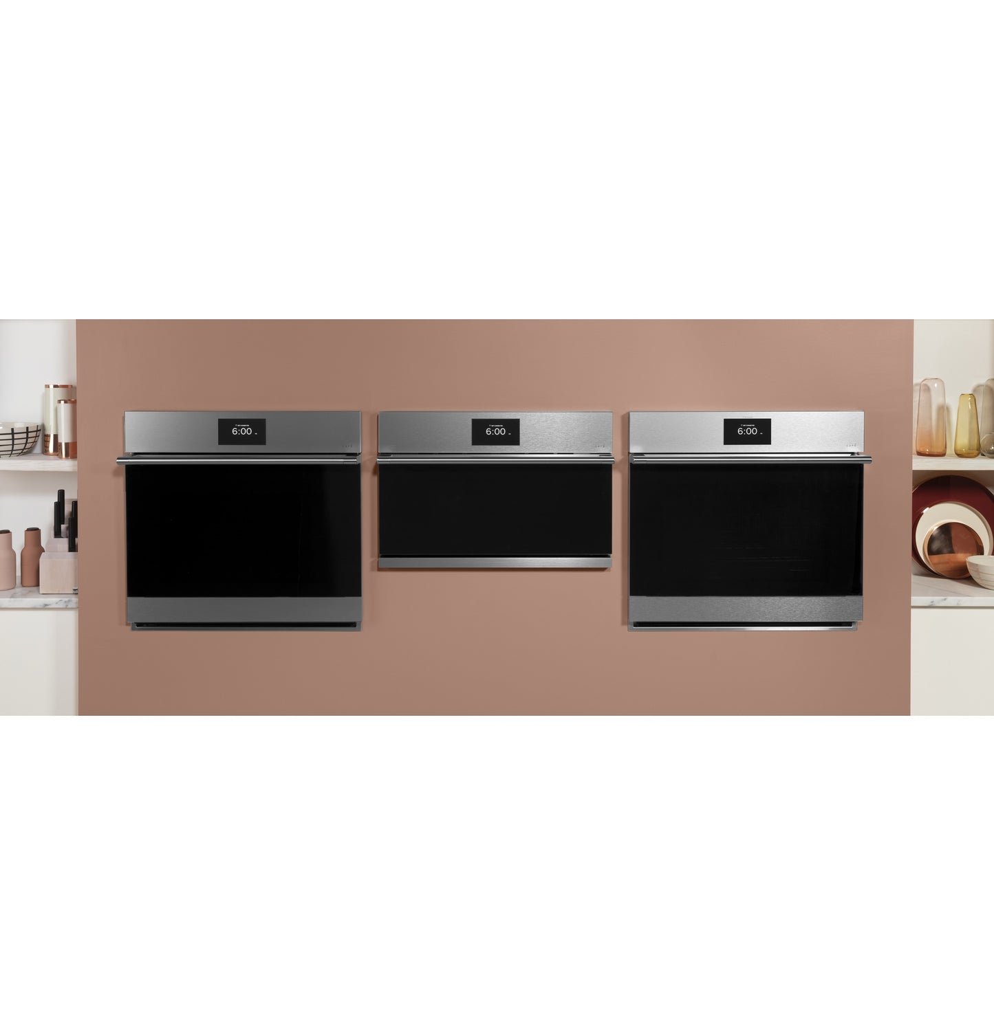 Three stainless steel wall ovens with digital displays mounted on a light brown kitchen wall in appliances setting