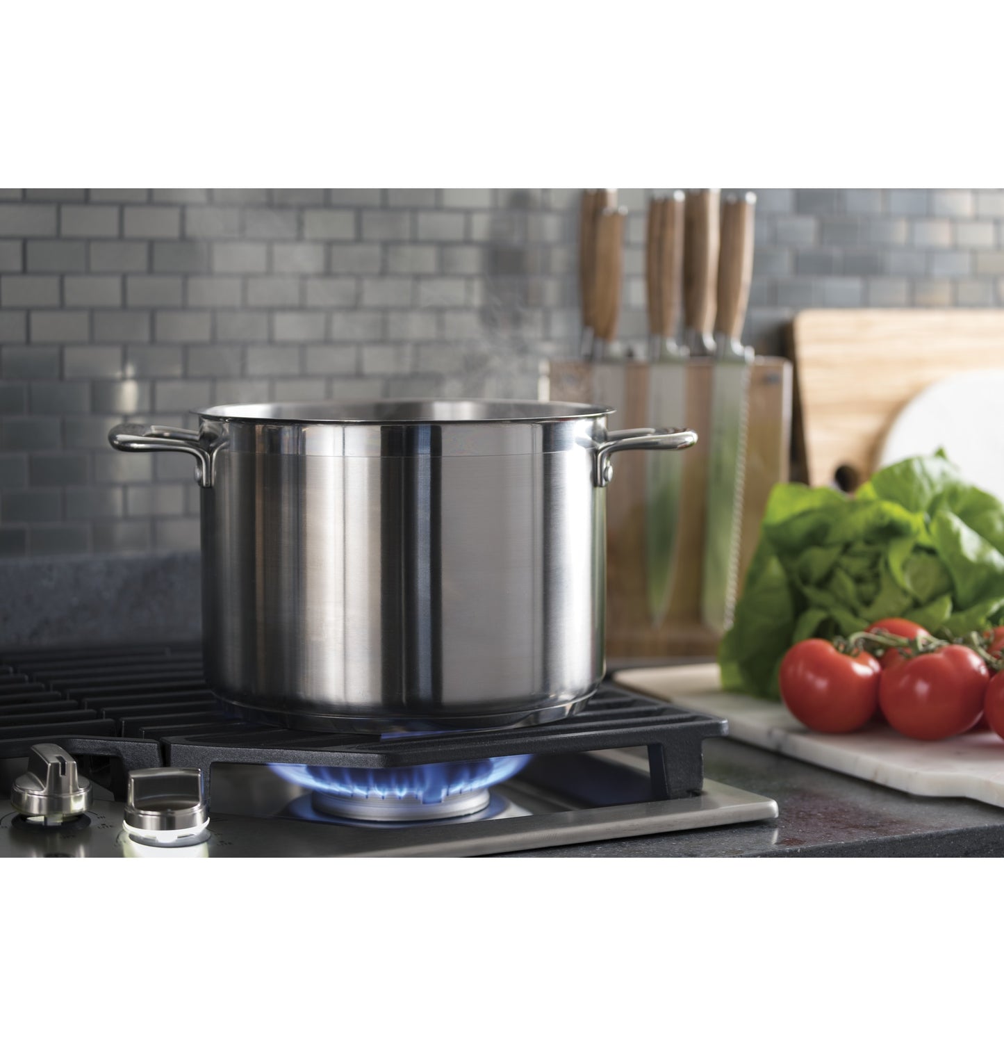 Stainless steel pot heating on a gas cooktop with fresh vegetables and knives in a modern kitchen setting